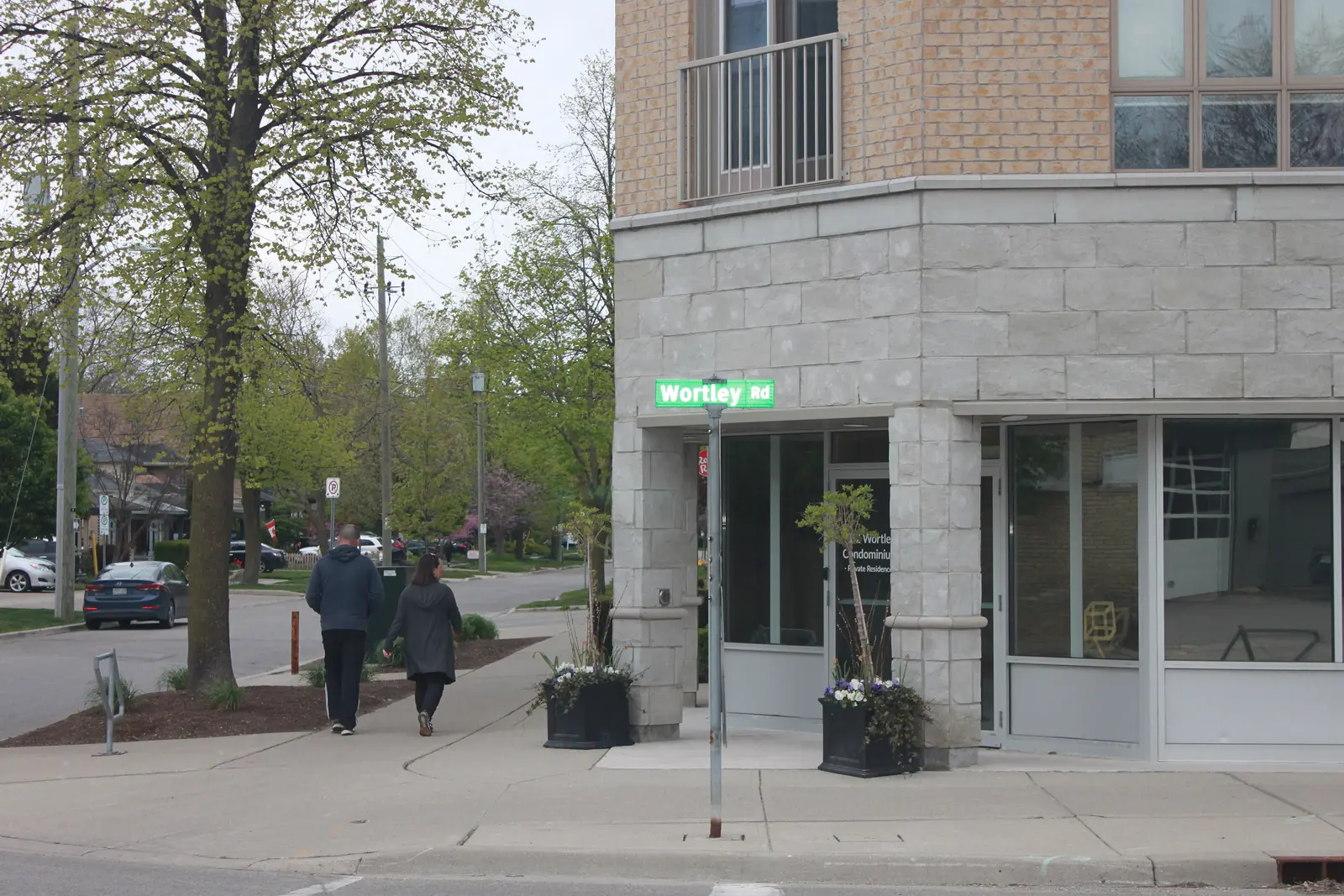 The corner of Wortley Road and Bruce Street in Wortley Village, London, Ontario, with a stone commercial building, a Wortley Rd street sign, and two people walking away on the sidewalk.